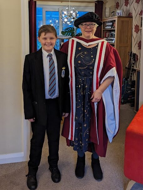 Photograph of an 11 year old boy in school uniform and a woman in a graduation gown and hat with a starry dress. Both are smiling